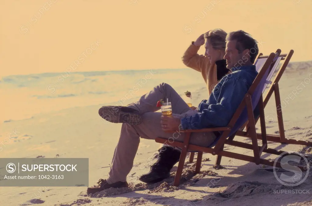Mid adult couple sitting in lounge chairs on the beach