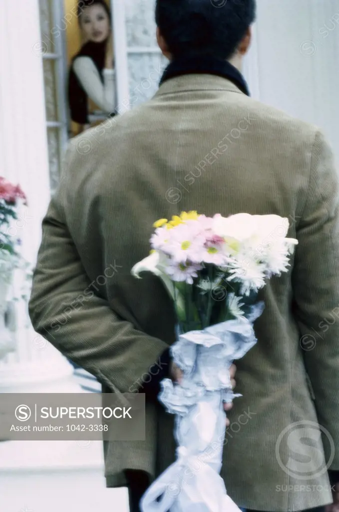 Rear view of a young man hiding a bouquet of flowers behind his back