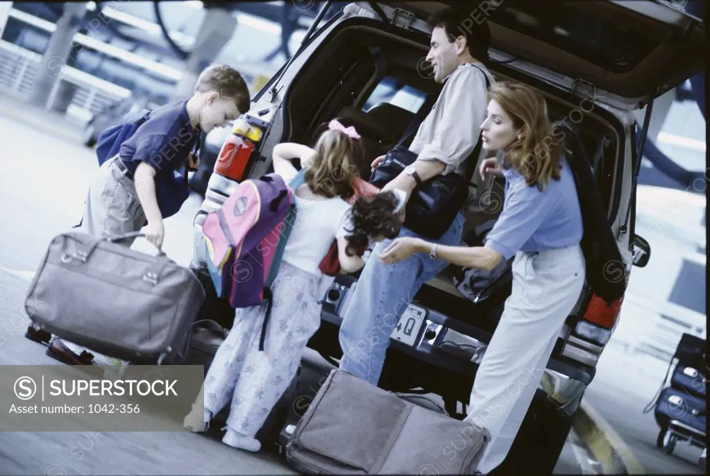 Parents with their son and daughter unloading luggage from a car