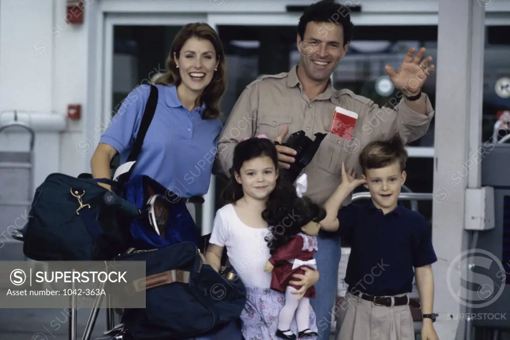 Portrait of parents with their son and daughter waving at an airport