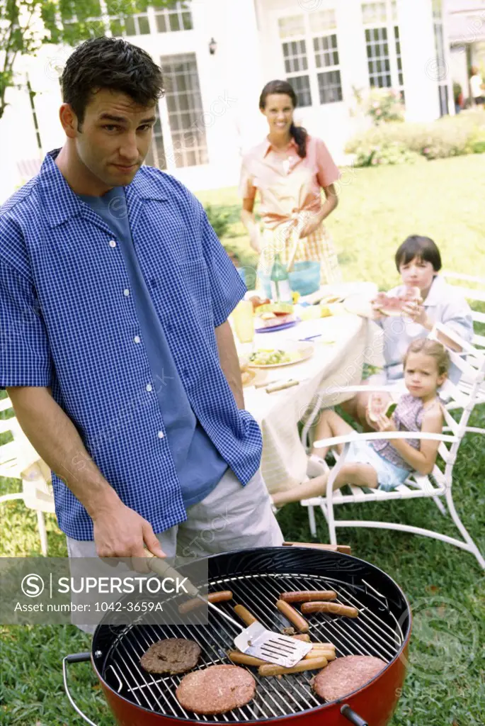 Father at a barbecue grill with his children behind him