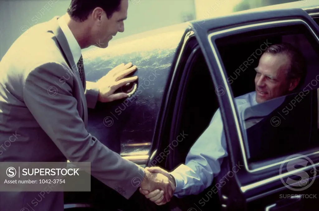 Two businessmen shaking hands sitting in a car