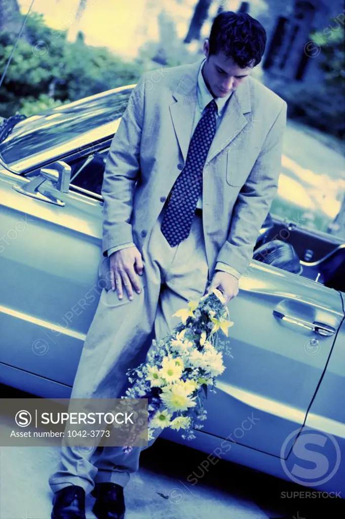 Young man standing against a car holding a bouquet of flowers