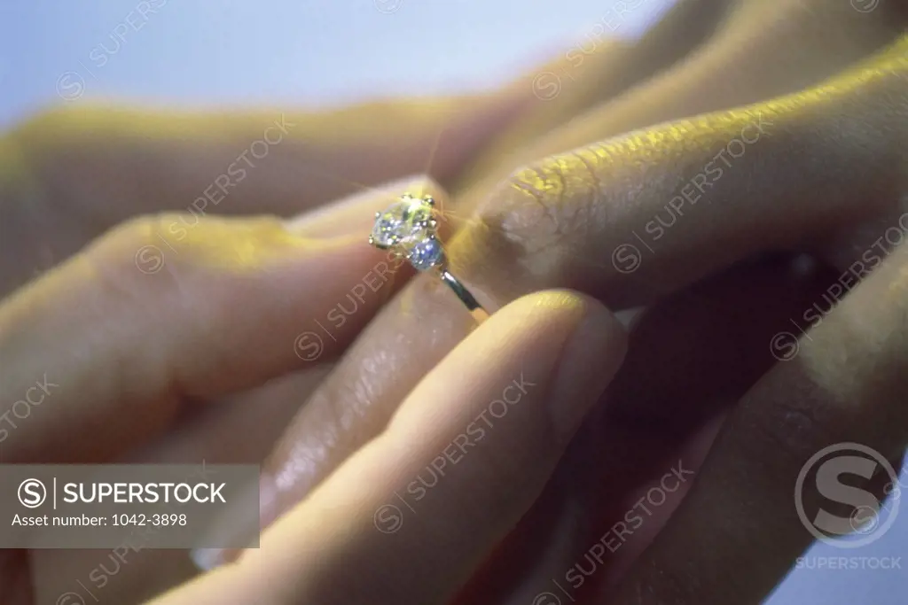 Close-up of a man putting on an engagement ring on a woman's finger