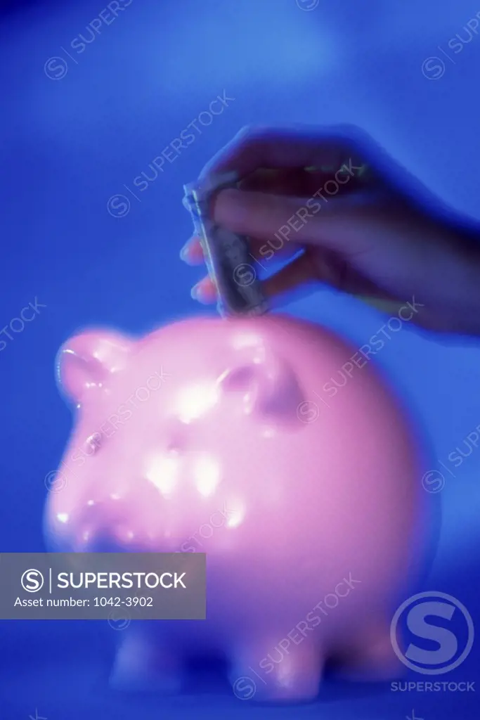 Person's hand dropping a dollar bill into a piggy bank