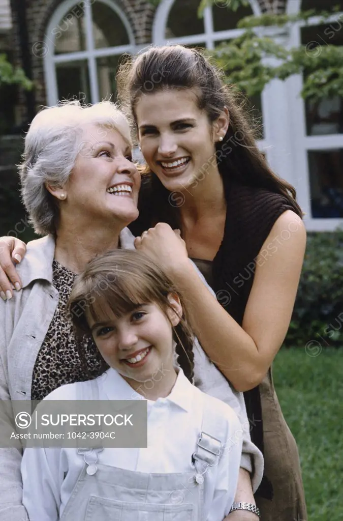 Portrait of a girl with her mother and grandmother standing on a lawn and smiling