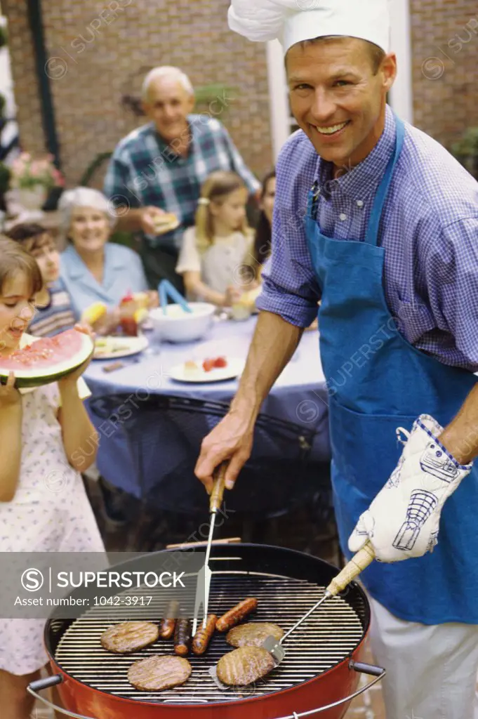 Young man cooking hot dogs on a barbecue grill