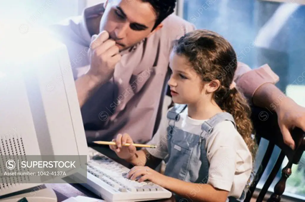 Young man with his daughter sitting in front of a desktop PC