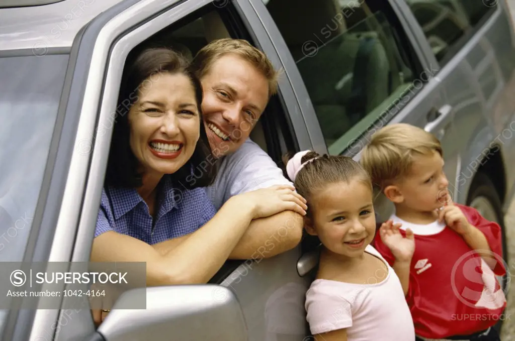 Portrait of parents sitting in a car with their son and daughter standing beside them