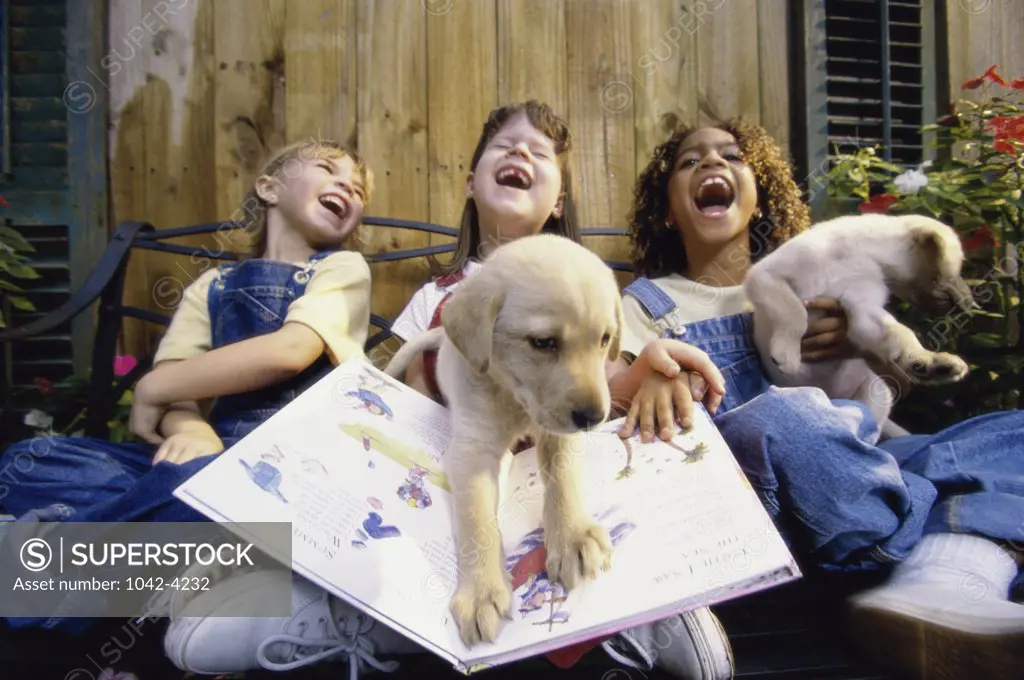 Three girls sitting together on a bench with their dogs