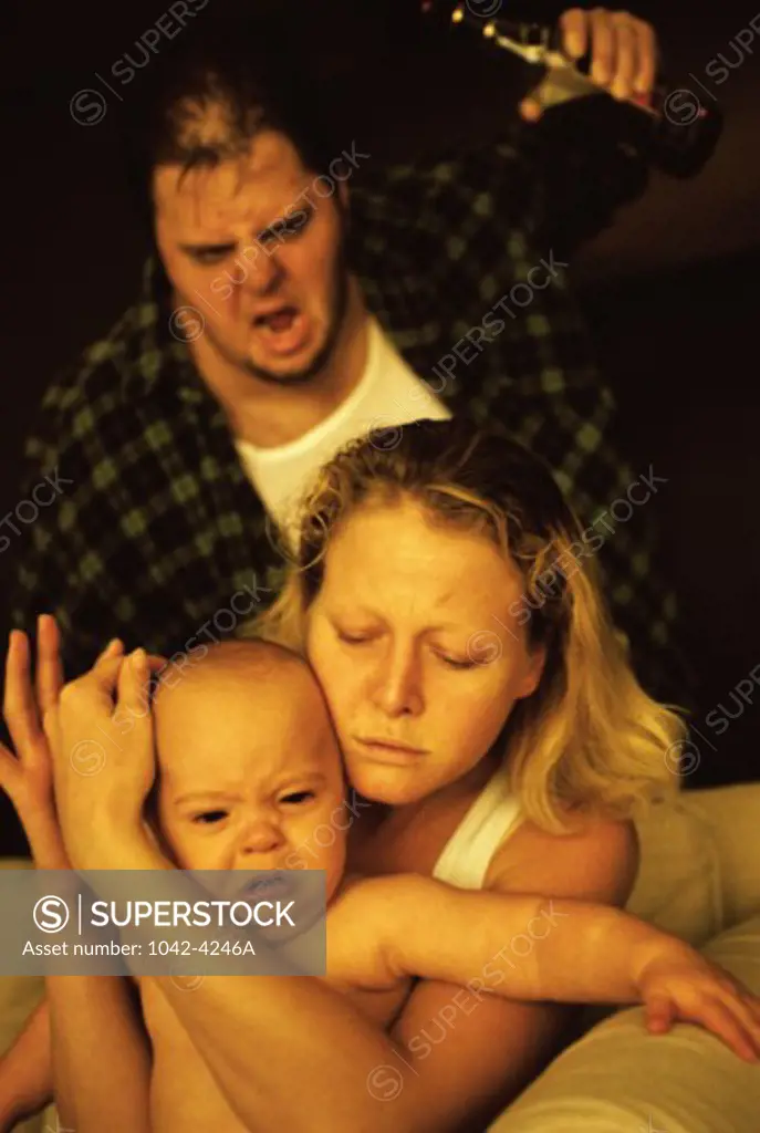 Mother holding her baby boy with a mid adult man shouting behind her