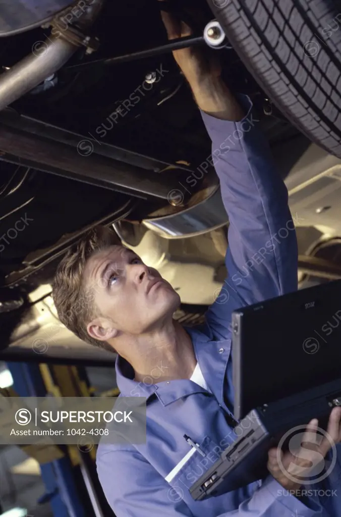 Young man standing under a car holding a laptop