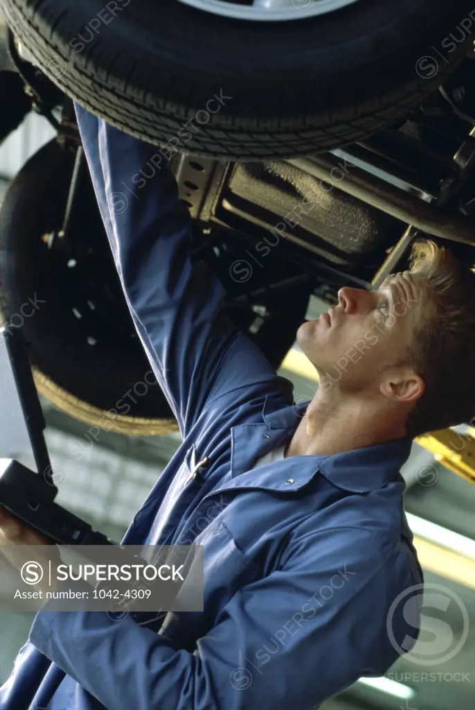 Side profile of a young man working under a raised car