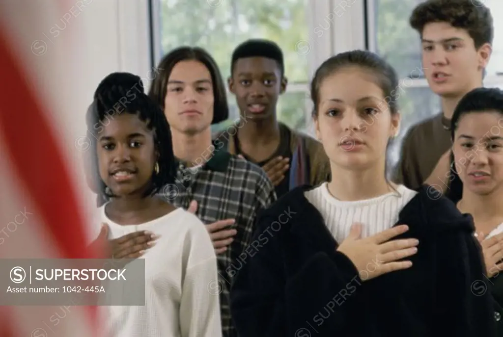 Group of teenagers saying the Pledge of Allegiance in front of an American flag in a classroom