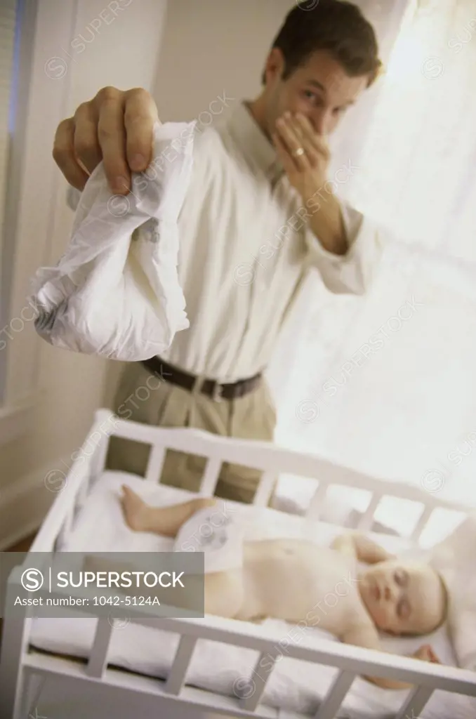 Father holding a diaper with his baby boy sleeping in a crib