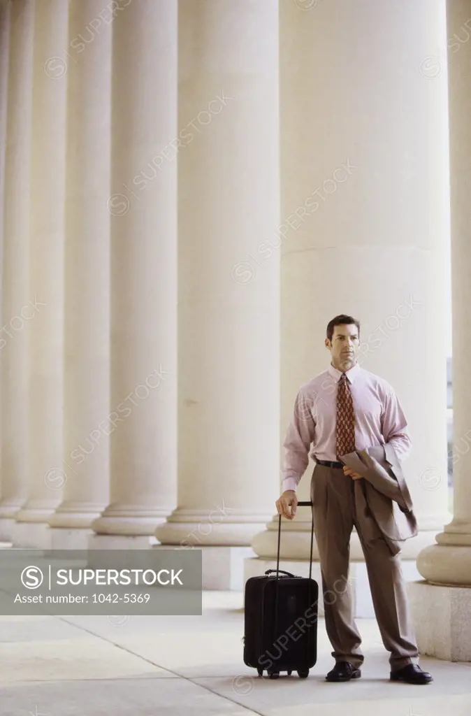 Businessman standing beside a column with luggage