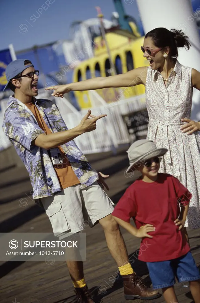 Mid adult couple pointing to each other walking with their son on a pier
