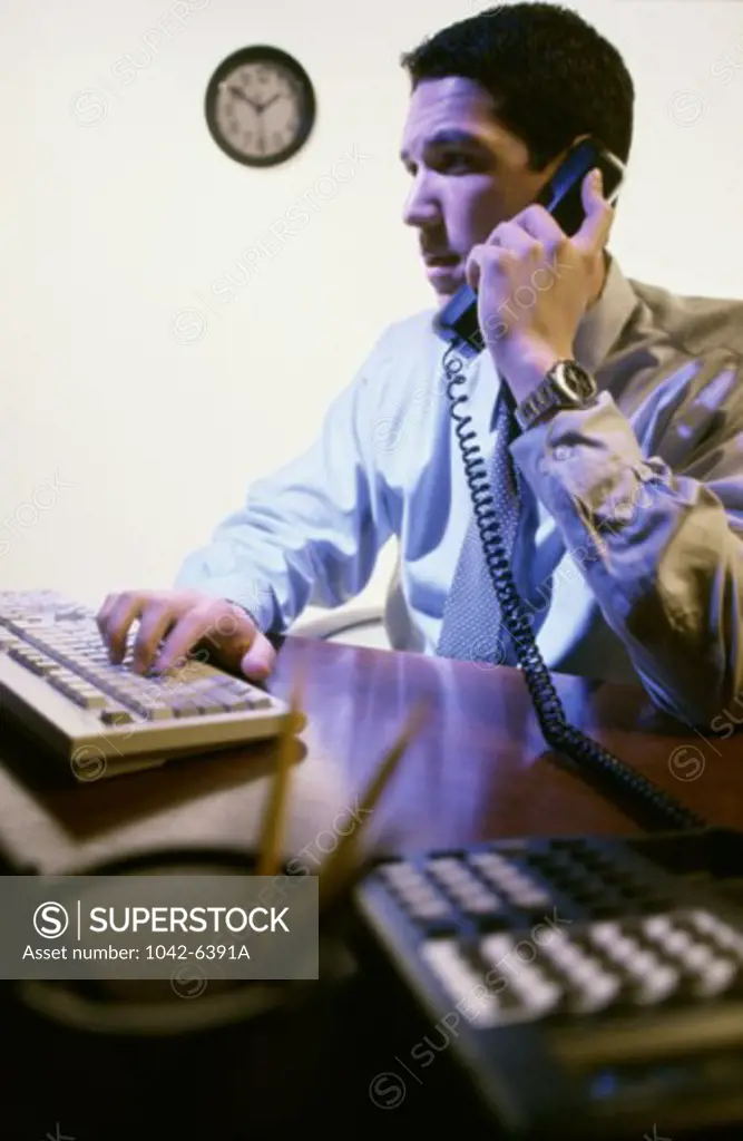 Side profile of a businessman working on a computer while talking on a telephone