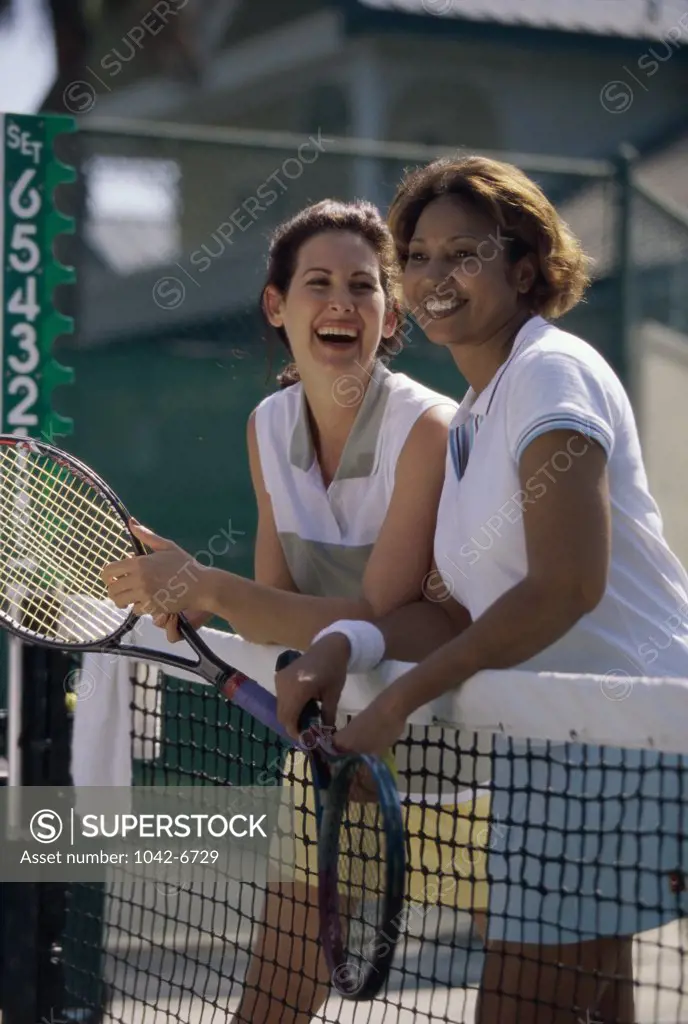 Two mid adult women standing against a tennis court net