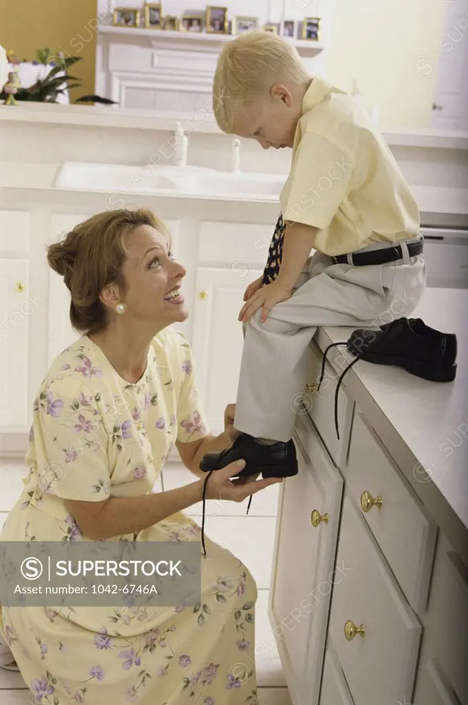 Side profile of a woman putting shoes on her son's feet