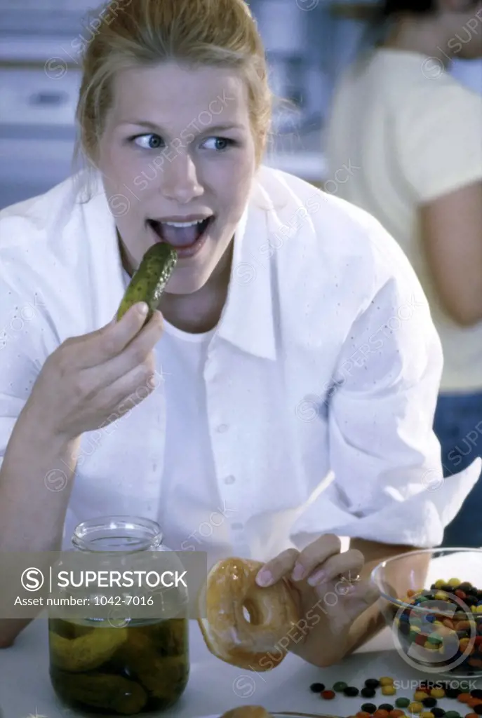 Young woman eating a pickle and holding a donut