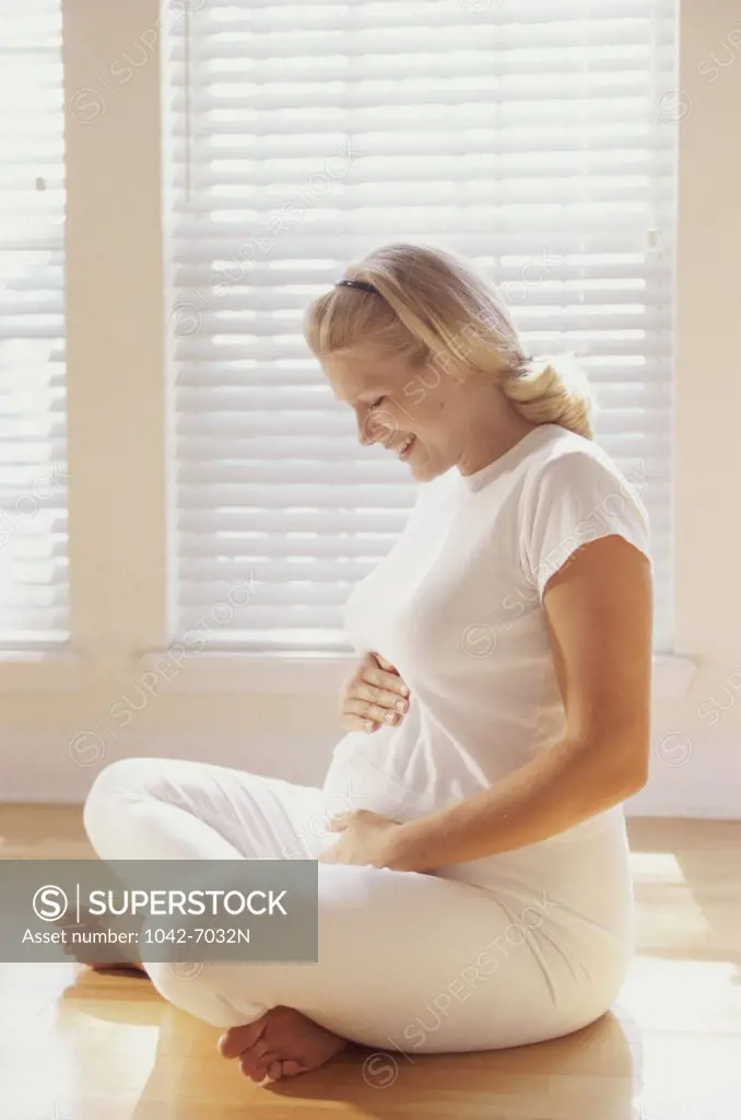Pregnant woman sitting on the floor touching her abdomen