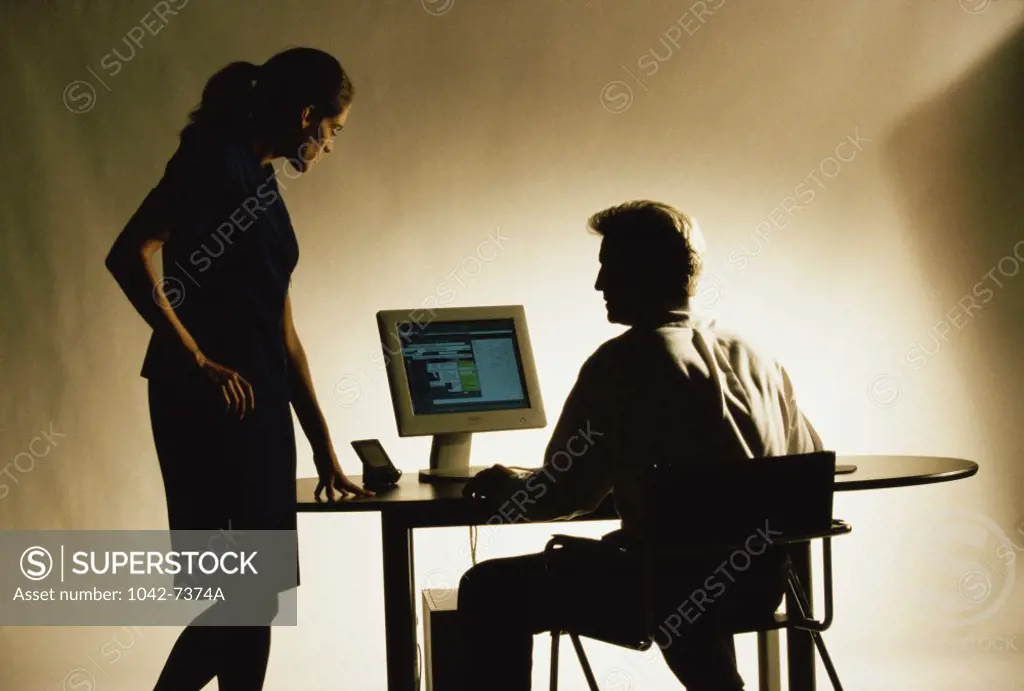 Silhouette of a businessman and a businesswoman in front of a computer monitor