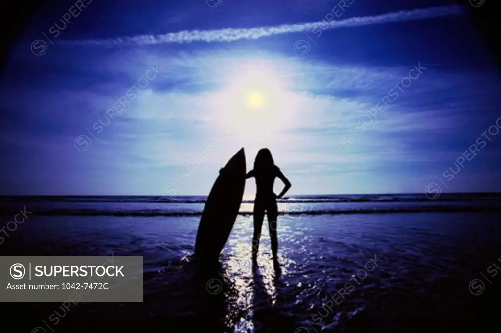 Silhouette of a woman holding a surfboard on the beach