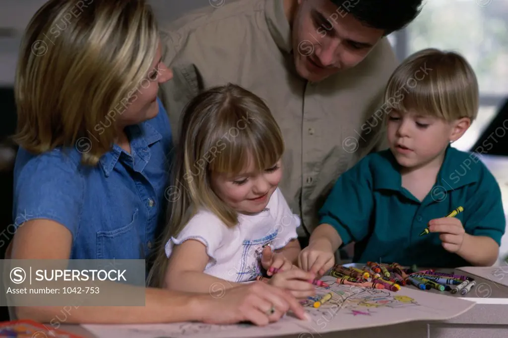 Parents helping their son and daughter to color using crayons