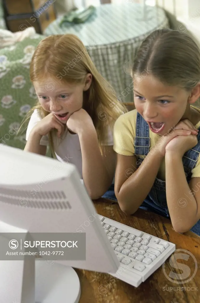 Two girls looking surprised at a computer monitor