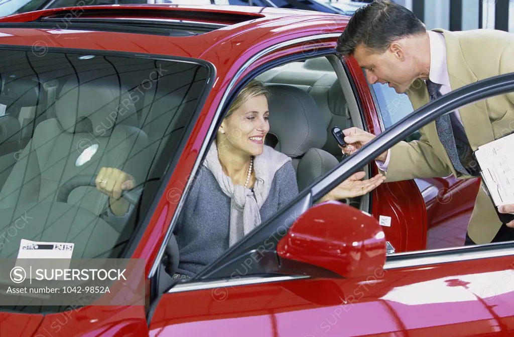 Mid adult woman sitting in a car talking to a salesman in a showroom