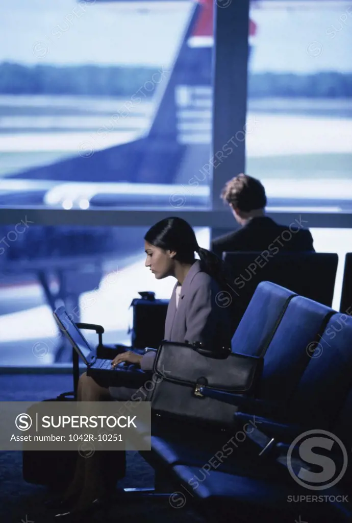 Side profile of a businesswoman sitting at an airport lounge working on a laptop