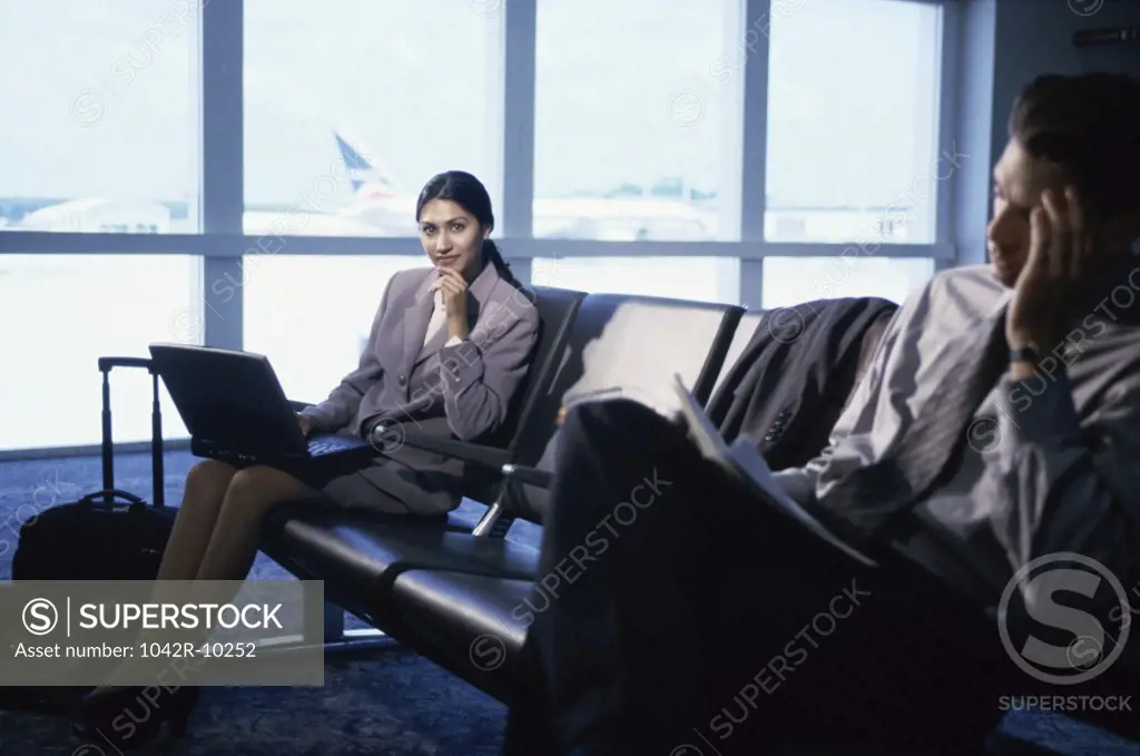 Side profile of a businesswoman and businessman sitting at an airport lounge
