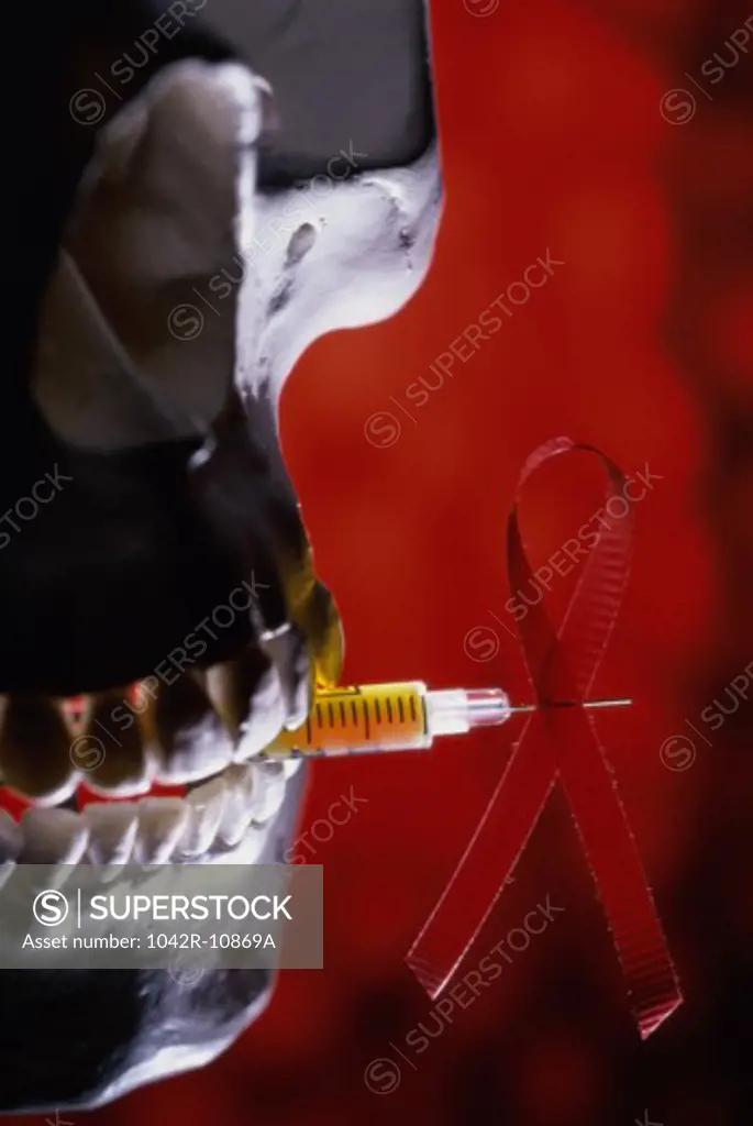 Close-up of a human skull biting a syringe with an AIDS awareness ribbon