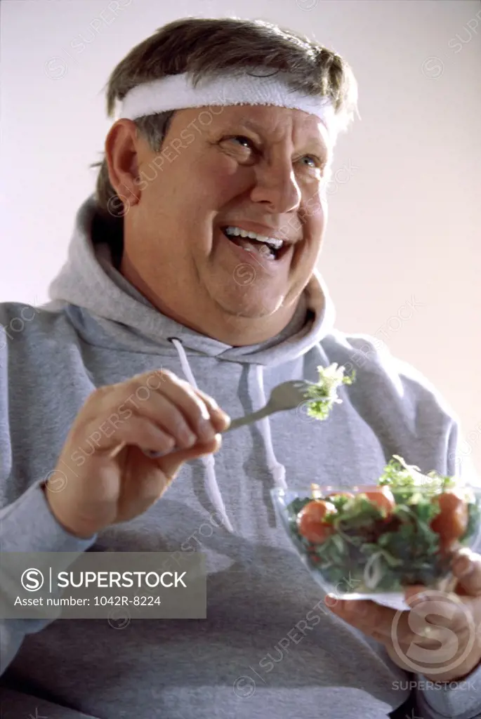 Mid adult man eating salad from a bowl with a fork