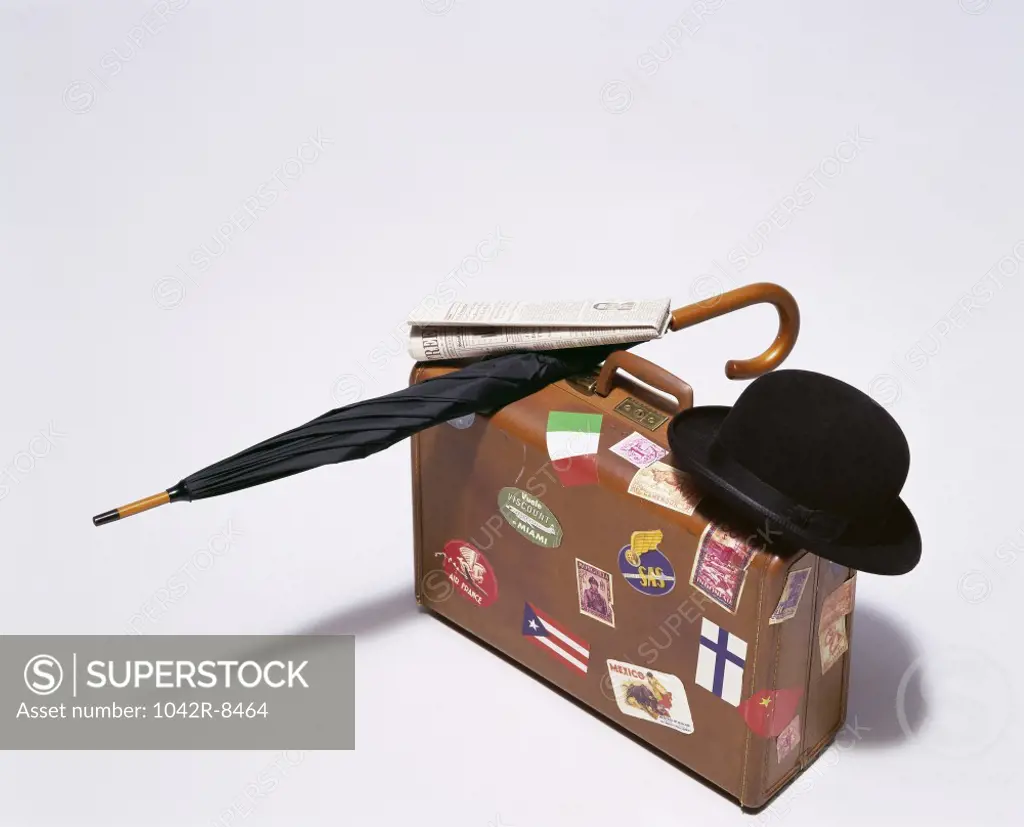 Hat with an umbrella and a newspaper on a suitcase