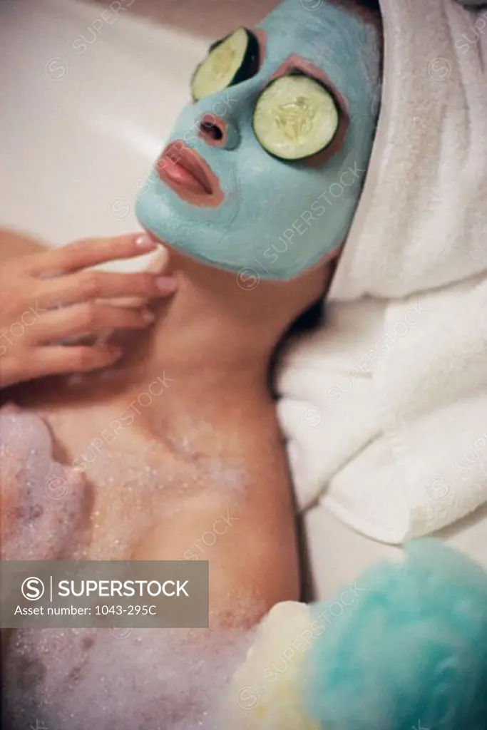 High angle view of a woman lying in a bubble bath wearing a facial mask