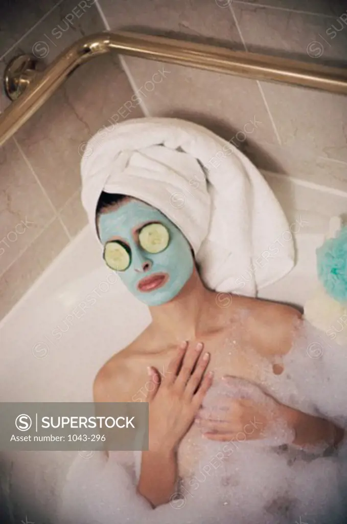 High angle view of a woman lying in a bubble bath wearing a facial mask