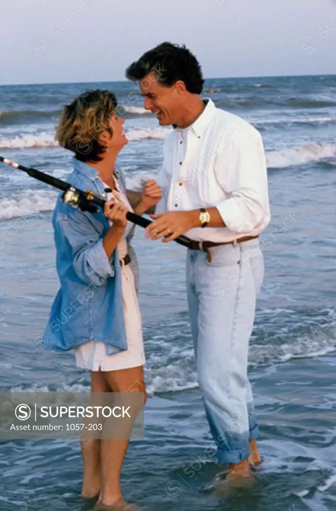 Mid adult couple standing on the beach and holding a fishing pole