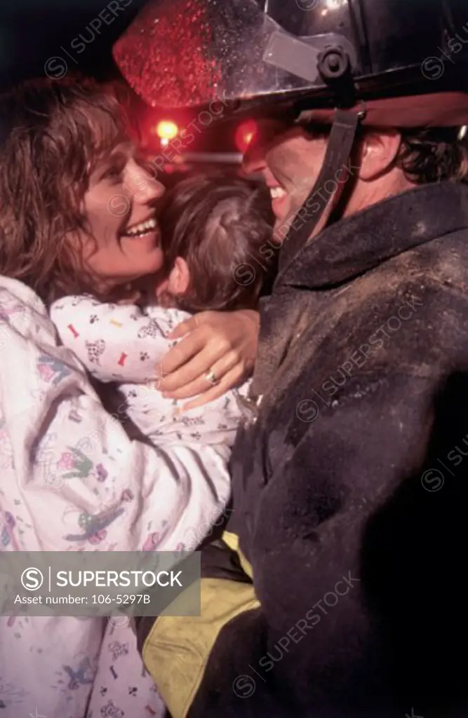 Side profile of a mid adult woman holding her baby girl and looking at a fireman