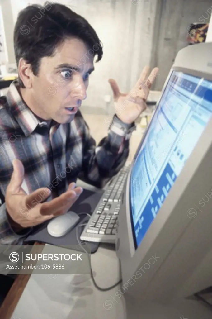 Close-up of a young man sitting in front of computer monitor and looking shocked