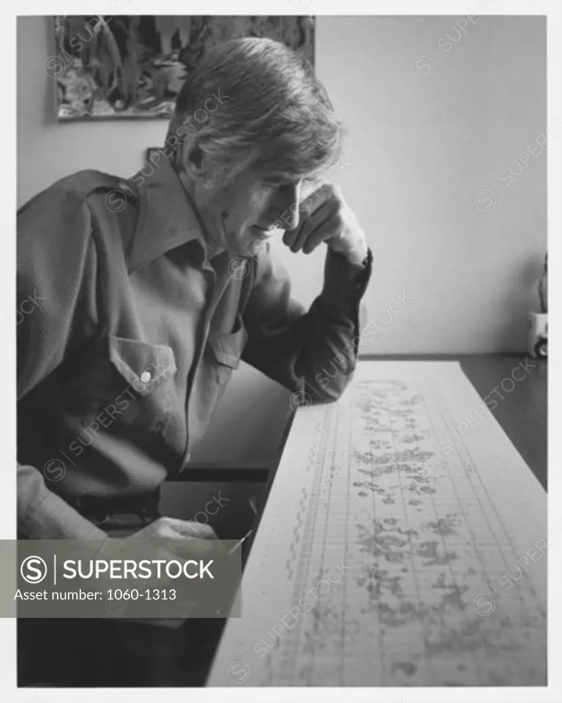 PORTRAIT OF JOHN ADKINS SEATED, LOOKING OVER SOLAR MAGNETIC CHART ON DESK.