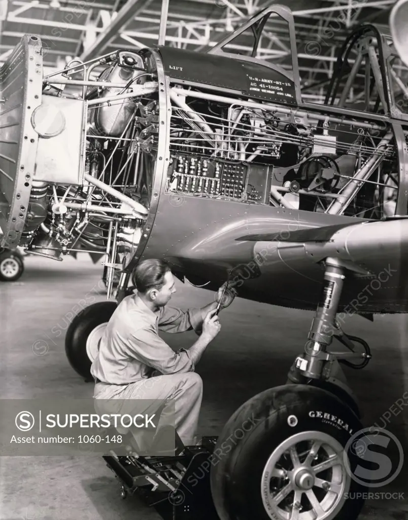 Side profile of an mechanic working on an aircraft in a factory.  Finished assembly. 1940