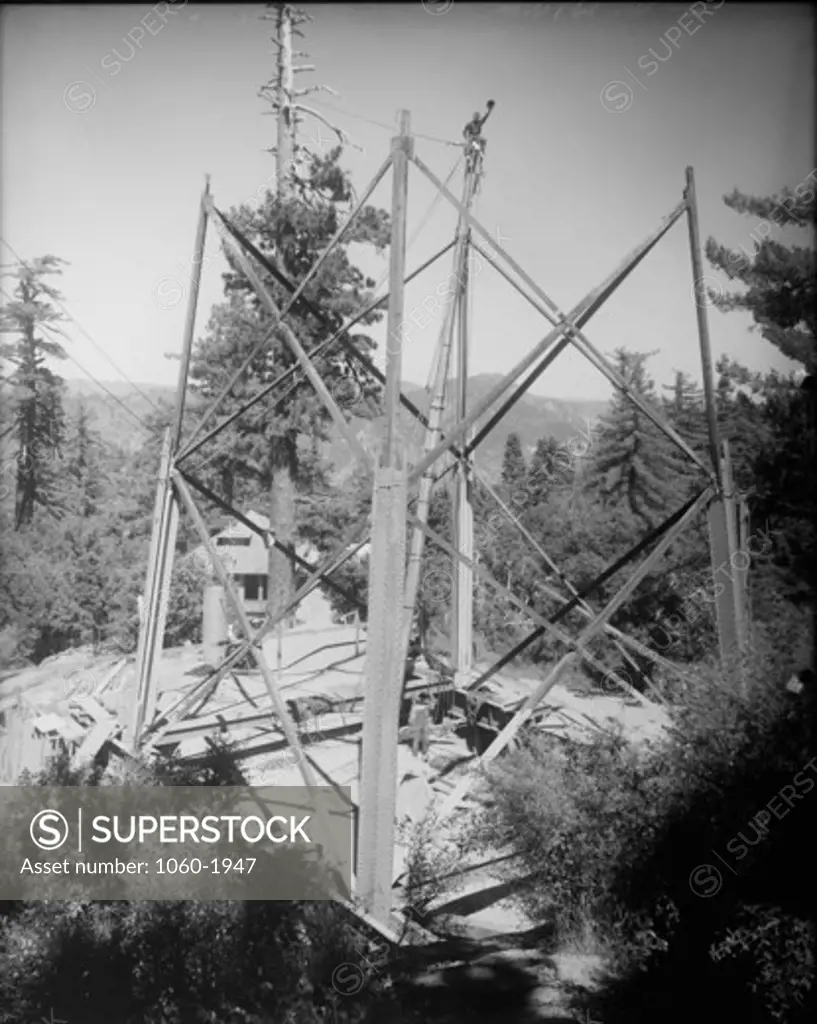 150-FOOT TOWER UNDER CONSTRUCTION, SECOND SECTION UP.  MAN SITTING ON TOP OF ONE OF THE TOWER LEGS.