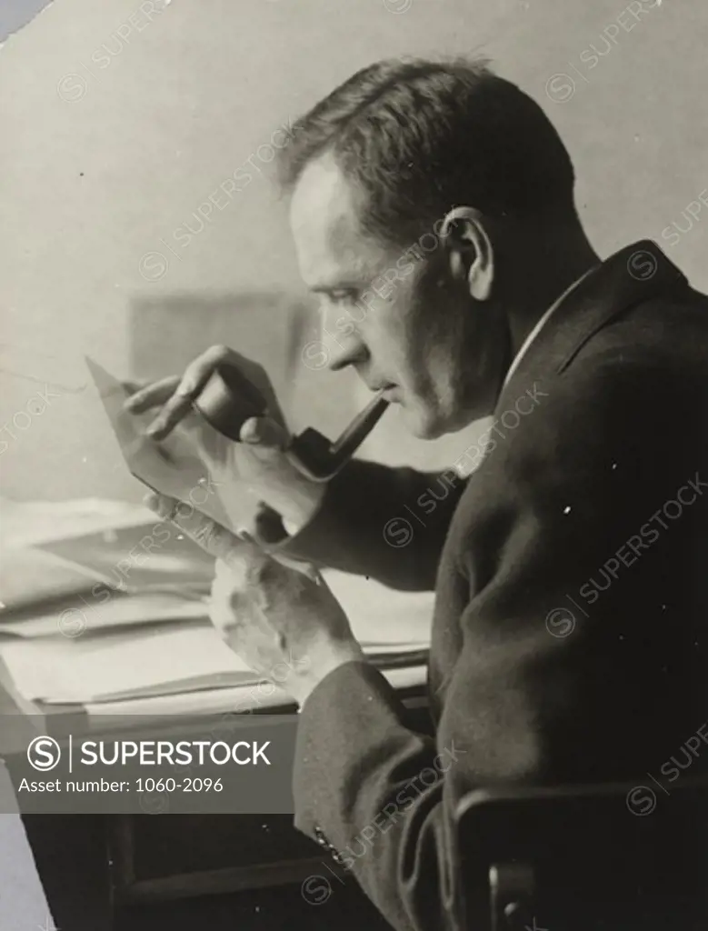 Edwin Powell Hubble looking through magnifying glass at photographic plate with pipe