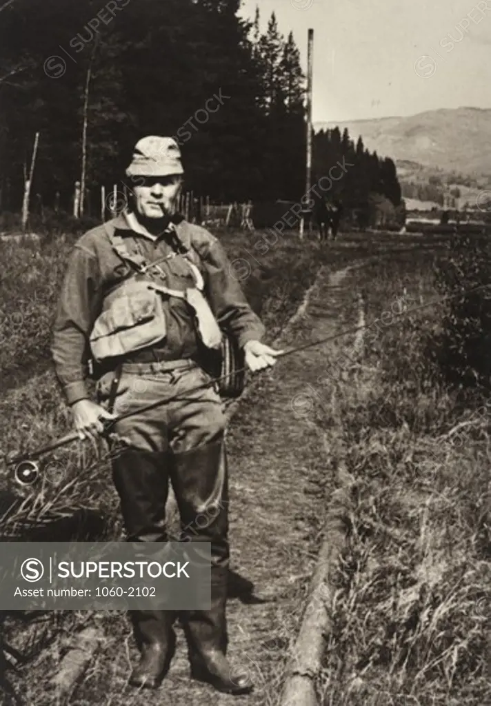 Edwin Powell Hubble standing on path, dressed in fishing gear, holding rod and smoking pipe