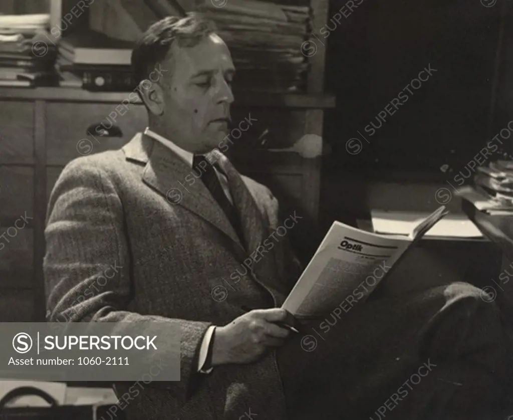 Portrait of Edwin Powell Hubble smoking pipe, sitting at desk and reading