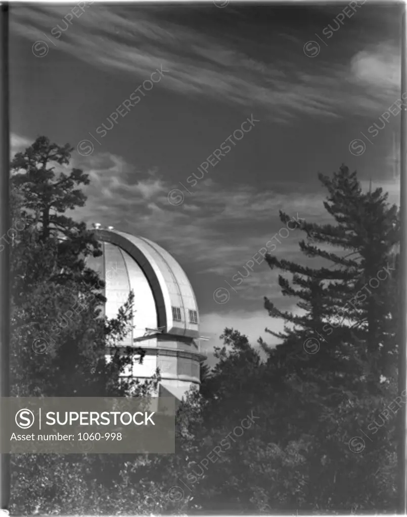 100-INCH TELESCOPE DOME, PARTIALLY VISIBLE BEHIND TREES.  SHUTTERS CLOSED, TOP HALF OF PHOTO SHOWS CLOUDY SKY.
