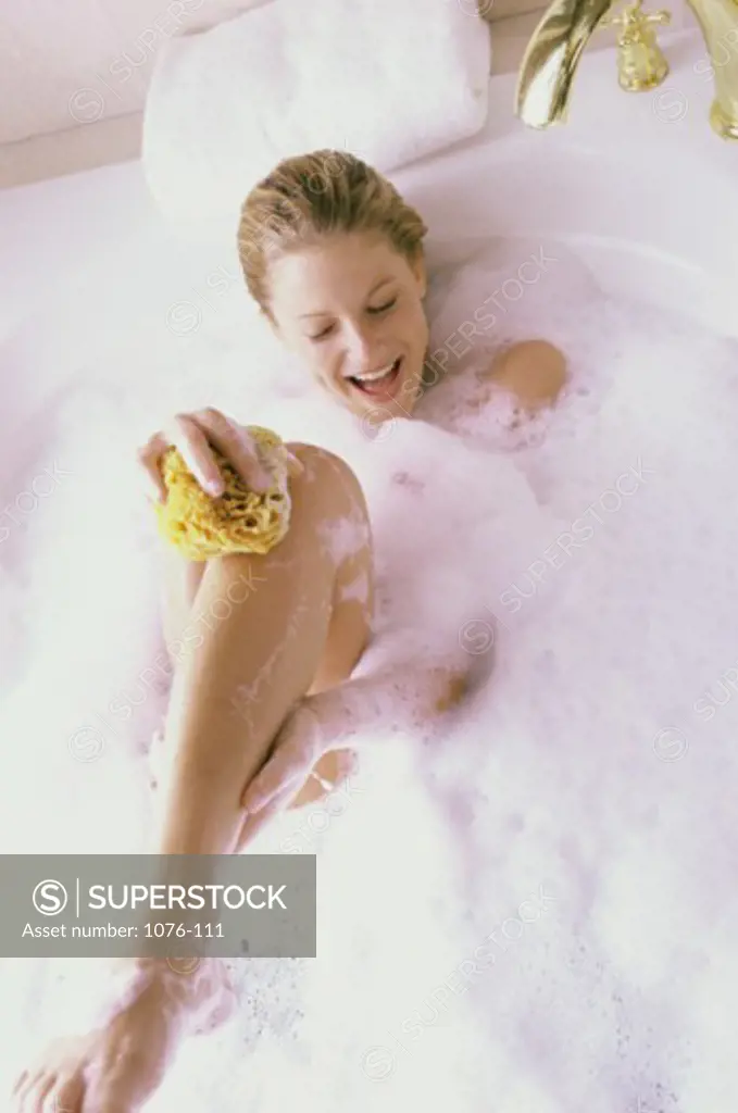 High angle view of a young woman using a loofah in a bubble bath