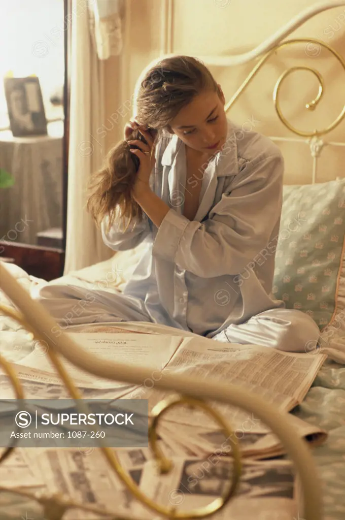 Young woman sitting on the bed reading a newspaper